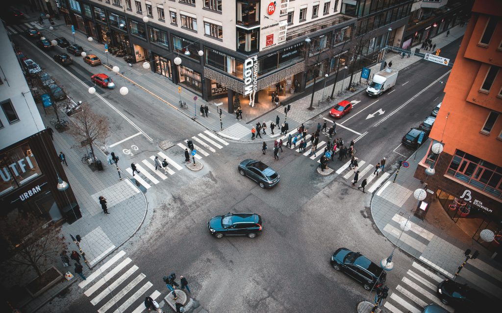 A bustling Stockholm street intersection with pedestrians and vehicles on a sunny day.